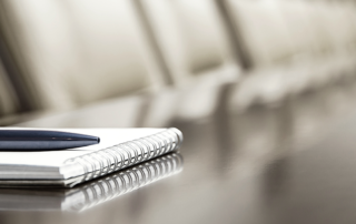 An image of a pen and notepad on a board room table.